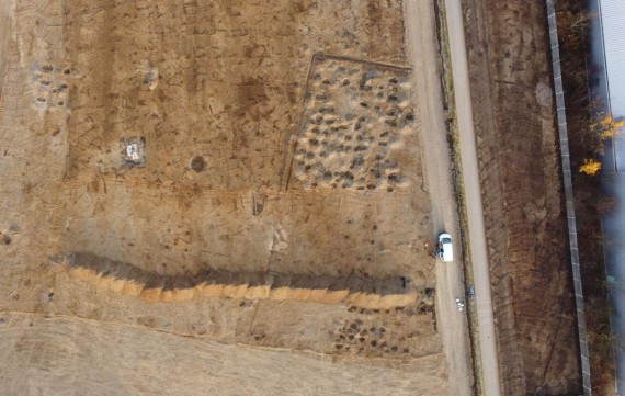 Luftbild einer Kiesfläche mit ausgegrabenen Pfostengruben, die als dunkle Flecken sichtbar sind.