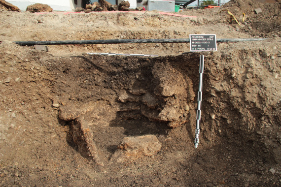 Grube im Boden, im Profil sichtbar: Tuffsteine als Brunnenkasten gesetzt. 